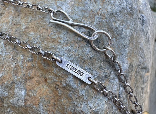 Silver chain necklace with 'STERLING' tag on a stone background